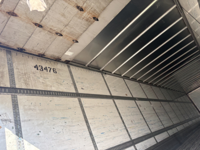 Inside of a trailer with metal walls, numbers 43476 printed on side, showing roll-up door mechanism and ribbed ceiling.