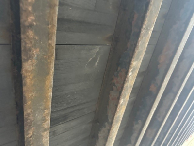 Trailer interior showing rusted vertical support beams and a ribbed metal wall, close-up view of roll door area.