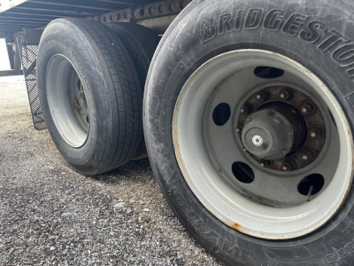 Truck trailer wheel assembly showing Bridgestone tire and white steel rim with lug nuts, side view of tandem axle.