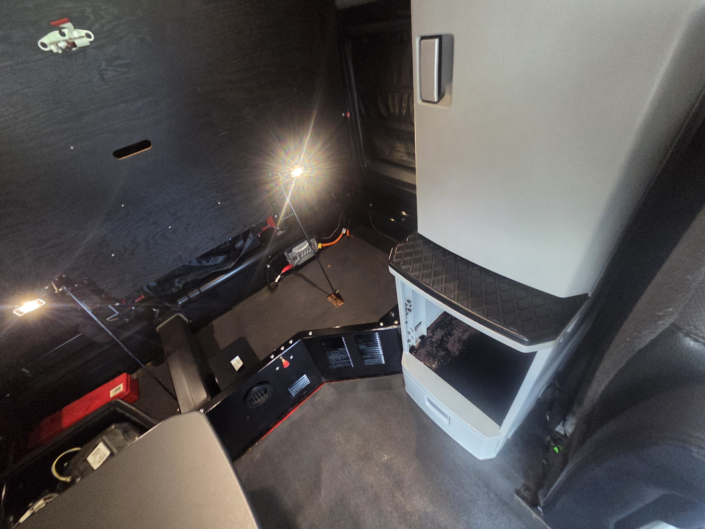 Kenworth T680 cab interior with driver's doorway, step, and dashboard area visible; some components and cables illuminated by a small light.