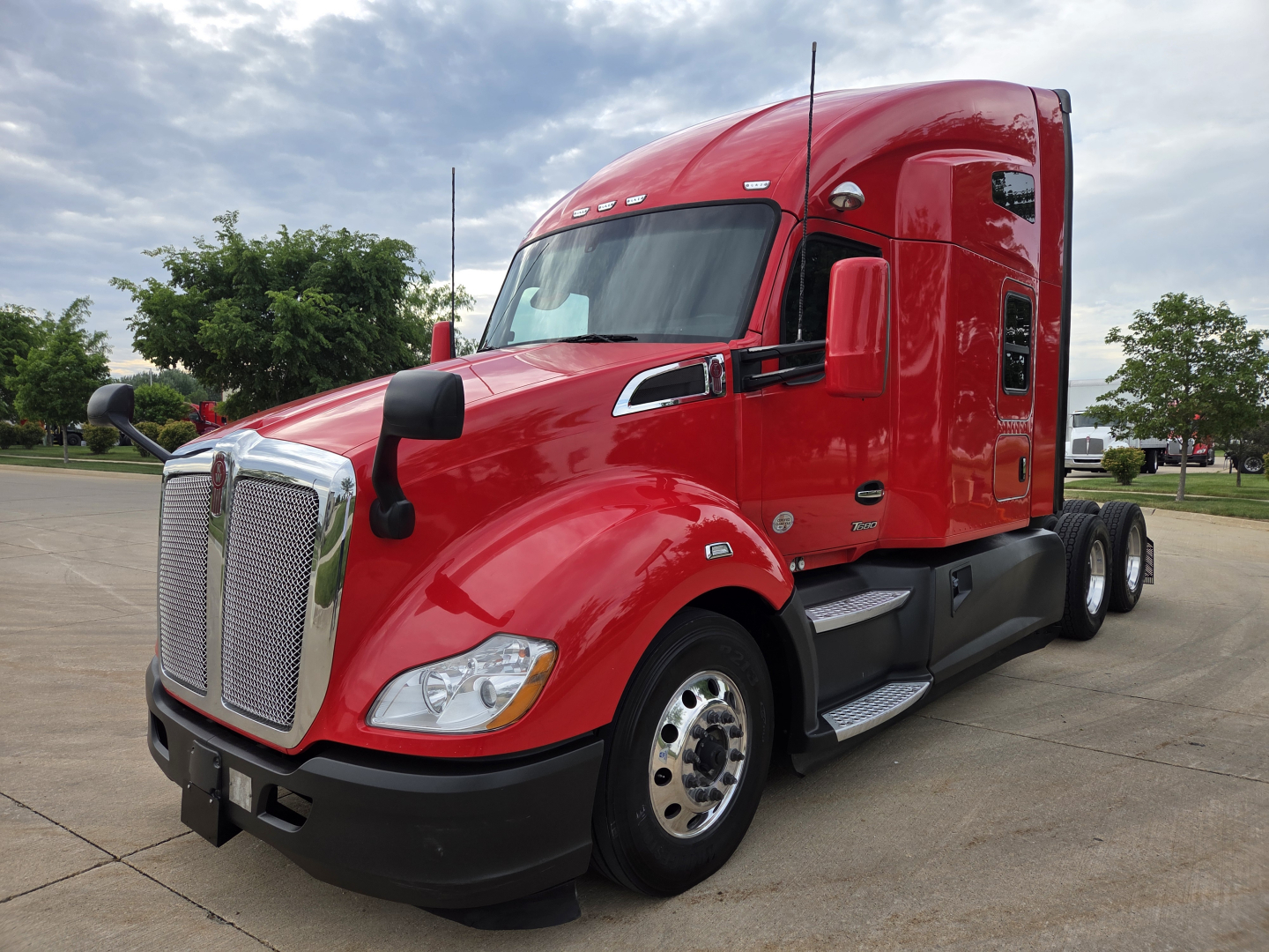 Kenworth T680 tractor in red color, side view showing front grille, headlights, and sleeper cab.