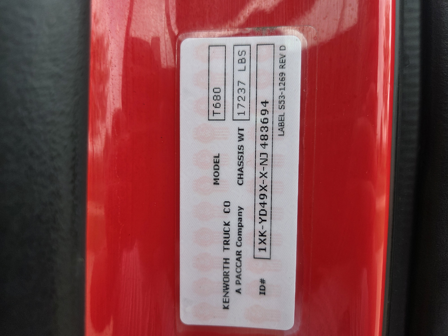 Kenworth T680 VIN sticker on door frame showing model T680, chassis weight 17237 LBS, label number 483694, and vehicle IDs; red painted surface around the label.