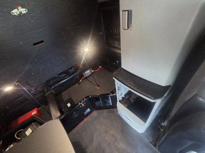 Kenworth T680 cab interior with driver's doorway, step, and dashboard area visible; some components and cables illuminated by a small light.