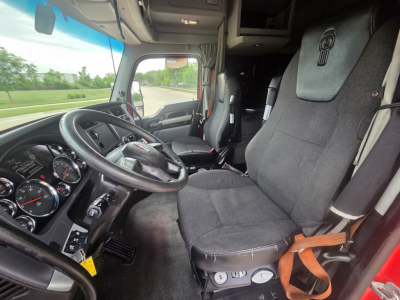 Kenworth T680 cab interior showing steering wheel, dashboard gauges, and driver seat with seat belt in view.