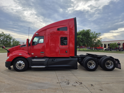 Kenworth T680 tractor in red with sleeper cab, side view showing rear axles and fuel tanks.