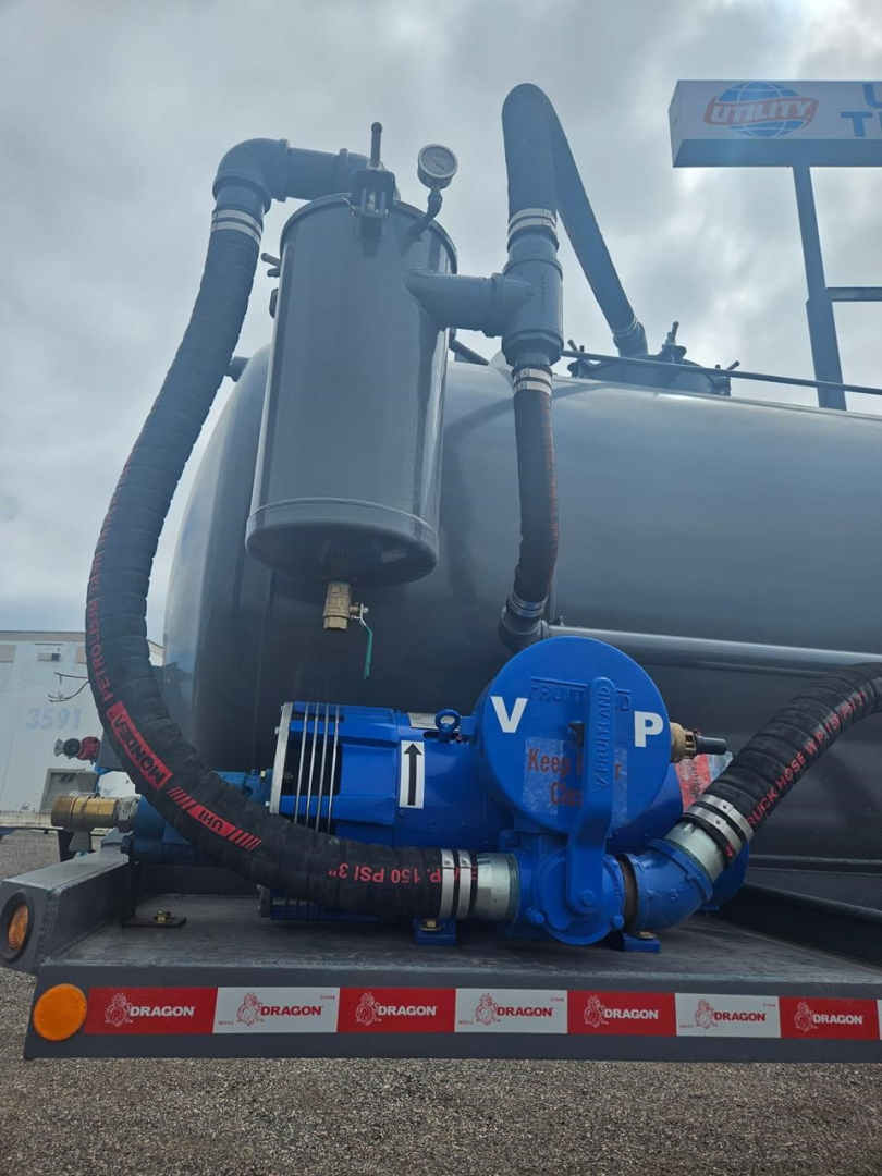 Blue rotary pump and hoses mounted on a large black vacuum trailer tank, with a blue diaphragm pump labeled V P and black insulated hoses coiled around.
