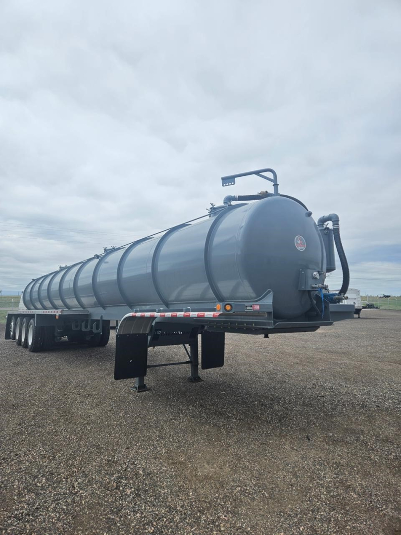 Vacuum trailer tank with multiple axles and cylindrical tank showing top-mounted plumbing and rear discharge hose. Side rail, dual-axle wheels, and support legs visible.