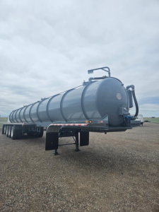 Vacuum trailer tank with multiple axles and cylindrical tank showing top-mounted plumbing and rear discharge hose. Side rail, dual-axle wheels, and support legs visible.