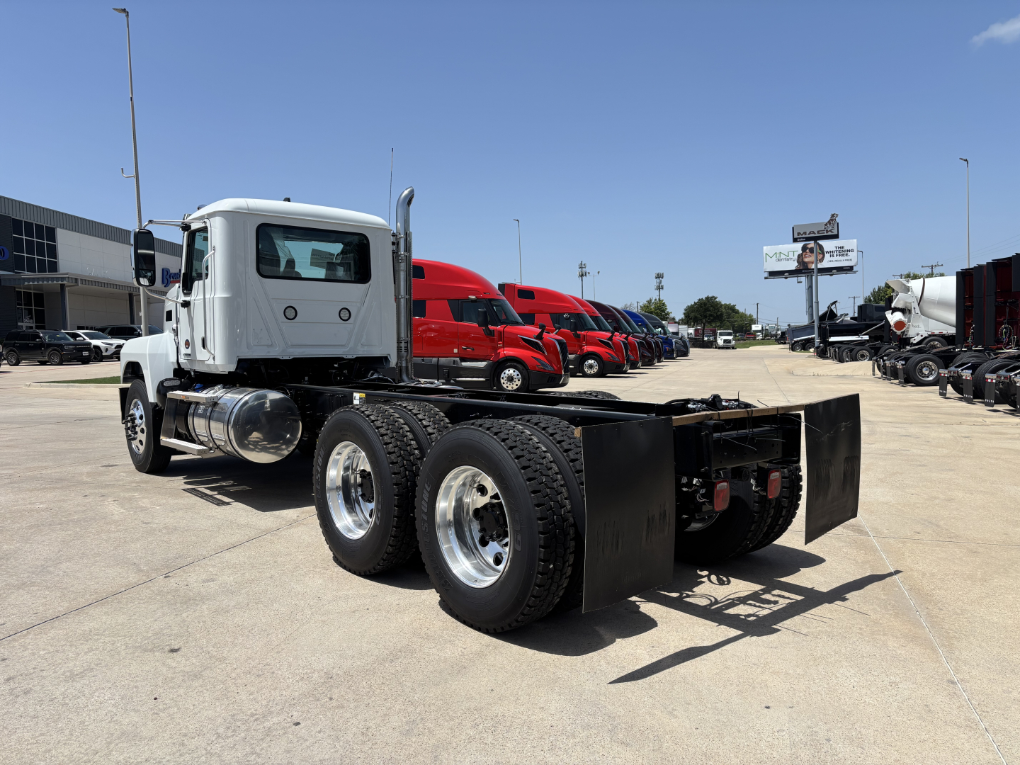 Truck chassis on display showing rear dual axles and frame with fifth wheel housing in a dealership lot.