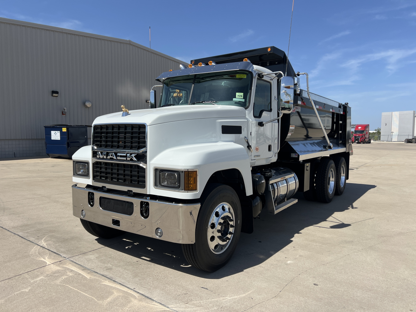 Mack PI64 dump truck with white cab and silver flatbed/ dump body, front view displaying grille, headlights, and dual rear axles.