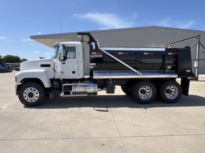 Dump truck showing 2027 Mack PI64 with white cab and black dump body, side view in parking lot.