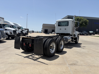 Semi truck chassis with cab and rear dual rear axles in a dealership lot; no visible branding text on the truck from this angle.