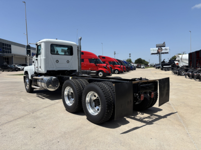 Truck chassis on display showing rear dual axles and frame with fifth wheel housing in a dealership lot.