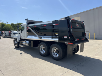 Dump truck rear and side view showing a black Mack PI64 dump body on a white truck chassis with dual rear axles and hydraulic dump mechanism.
