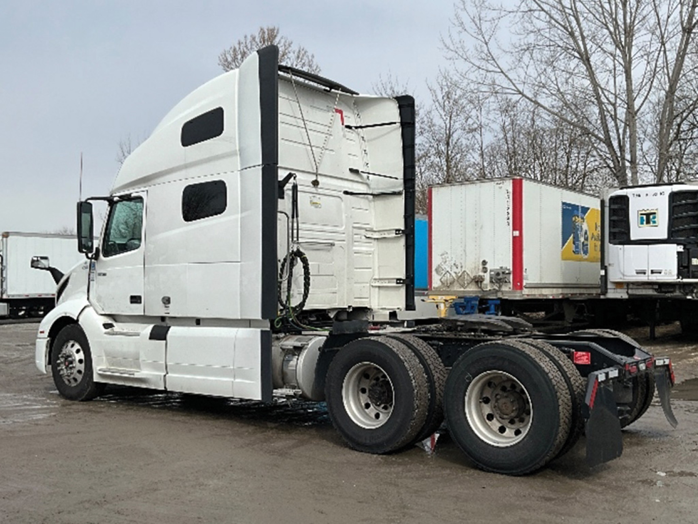 Volvo VNL 760 tractor cab in white seen in side view with dual rear axles and detached trailers in background.