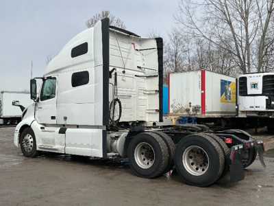 Volvo VNL 760 tractor cab in white seen in side view with dual rear axles and detached trailers in background.