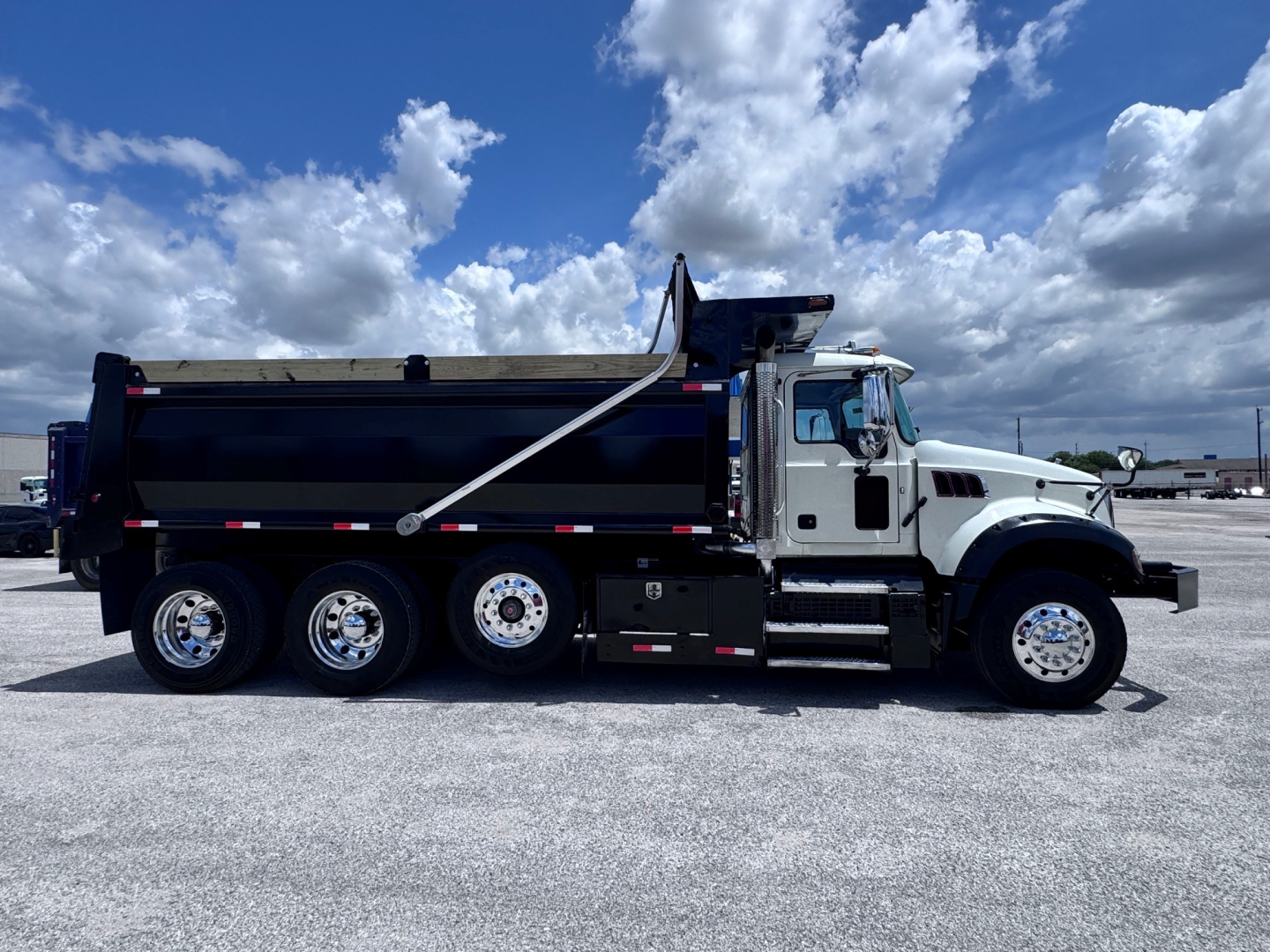 Dump truck showing Mack GR84F dump body with six wheels, black bed, white cab, side wedge, and chrome rims.