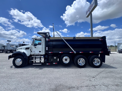 Dump truck side view showing Mack GR84F dump truck with black dump bed and white cab, three rear axles, and side rails.