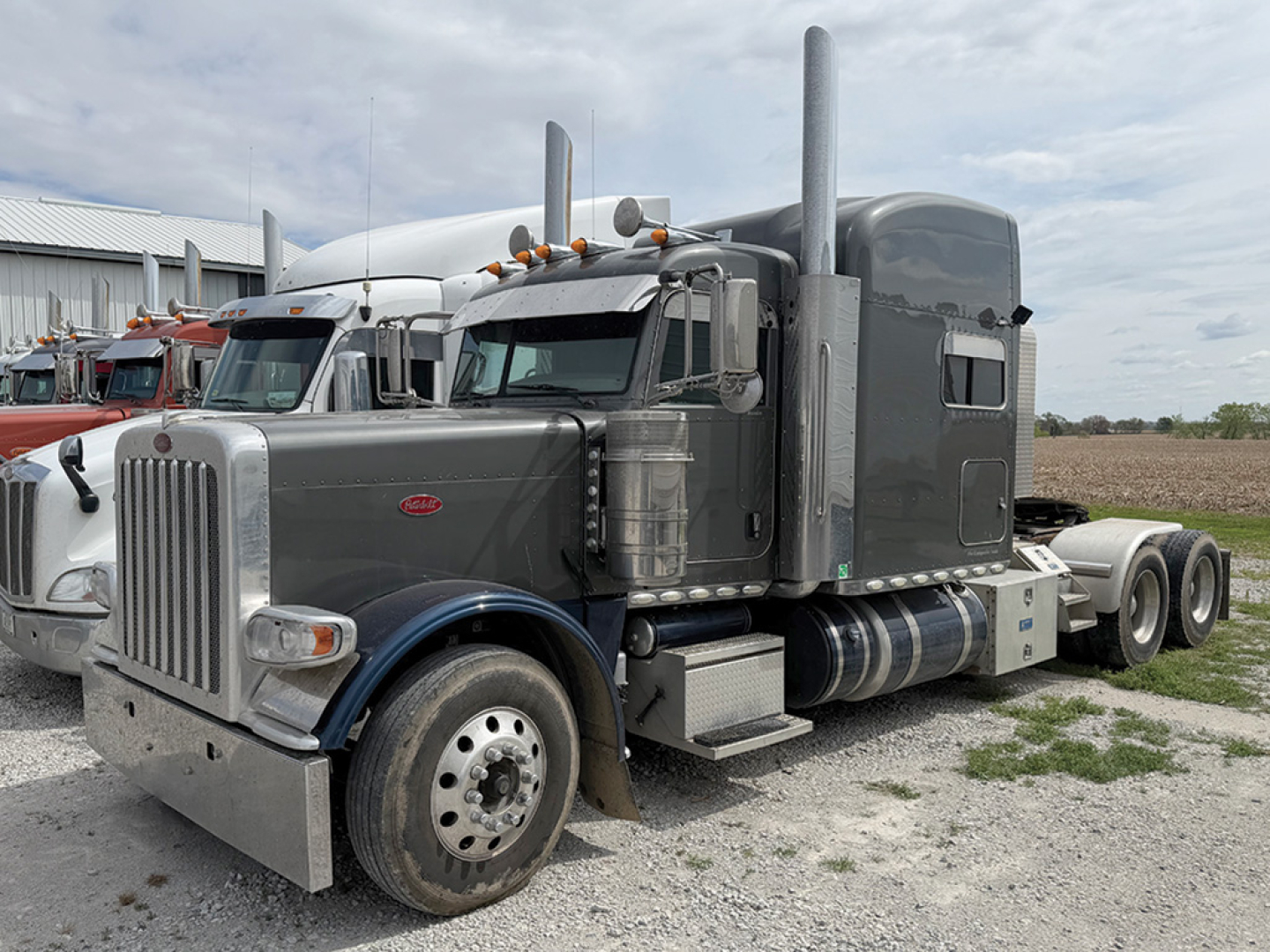 Peterbilt 389 UltraCab conventional Sleeper tractor in gray with tall sleeper and dual high exhaust stacks, front chrome grille, large round headlights, and dual rear axles on a gravel lot.