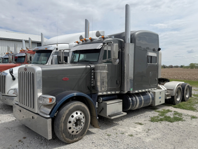 Peterbilt 389 UltraCab conventional Sleeper tractor in gray with tall sleeper and dual high exhaust stacks, front chrome grille, large round headlights, and dual rear axles on a gravel lot.
