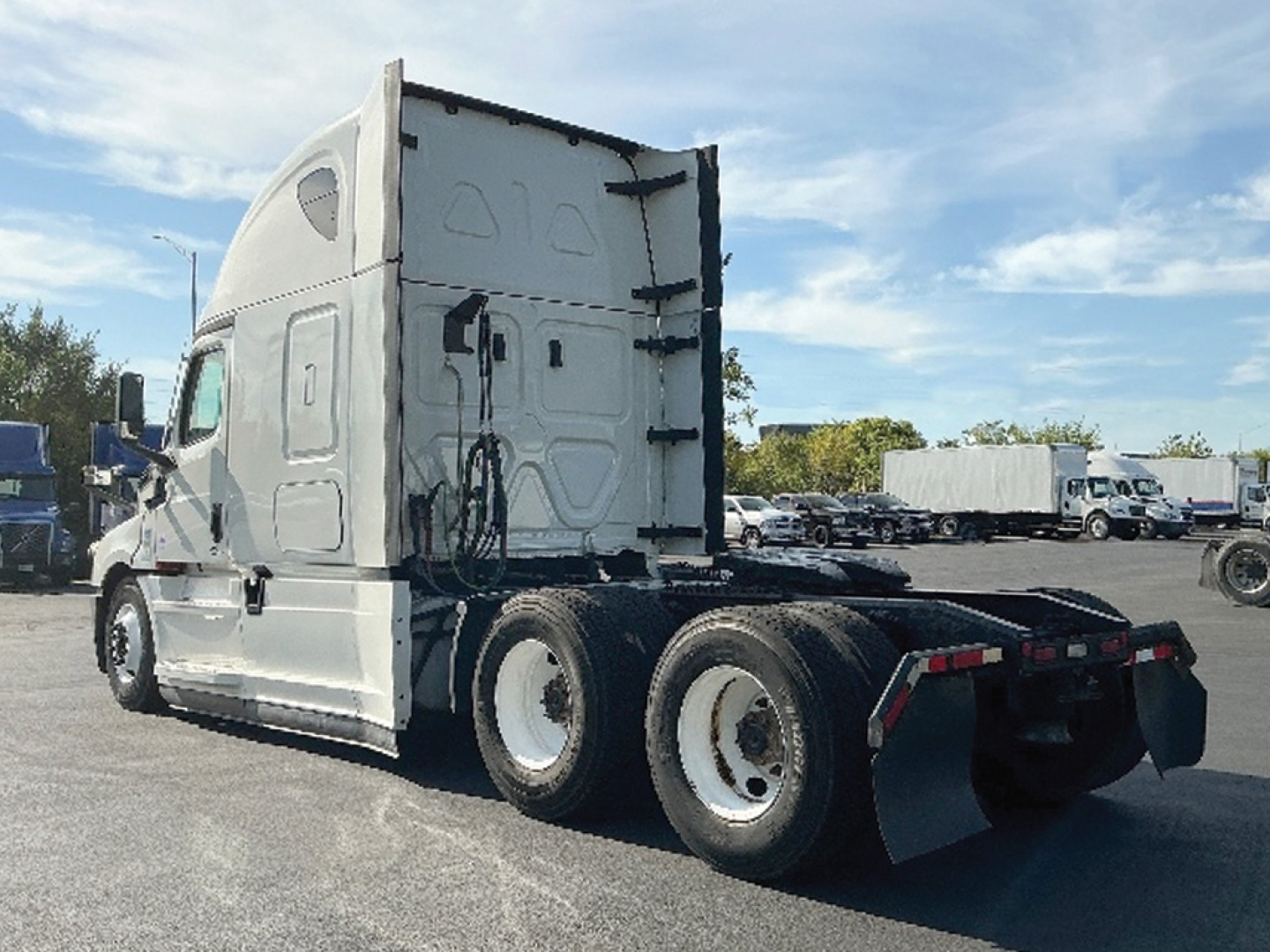 Truck rear view of a used 2021 Freightliner Cascadia126 tractor with sleeper cab, triple rear axles, and fifth wheel, in a dealership lot.