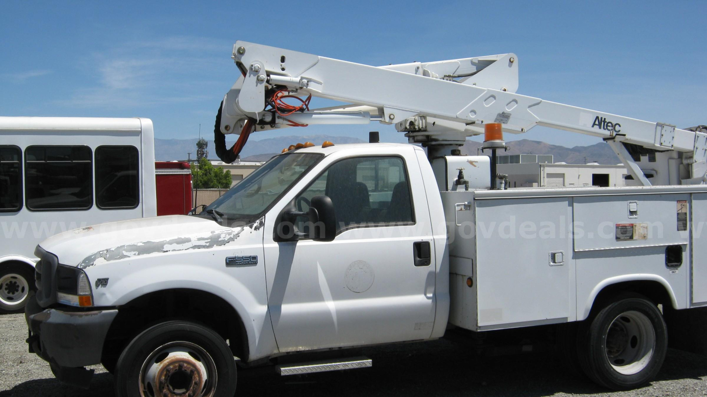 2002 Ford F-550 crew cab service truck with boom lift and Altec bucket truck body, side view showing utility compartments