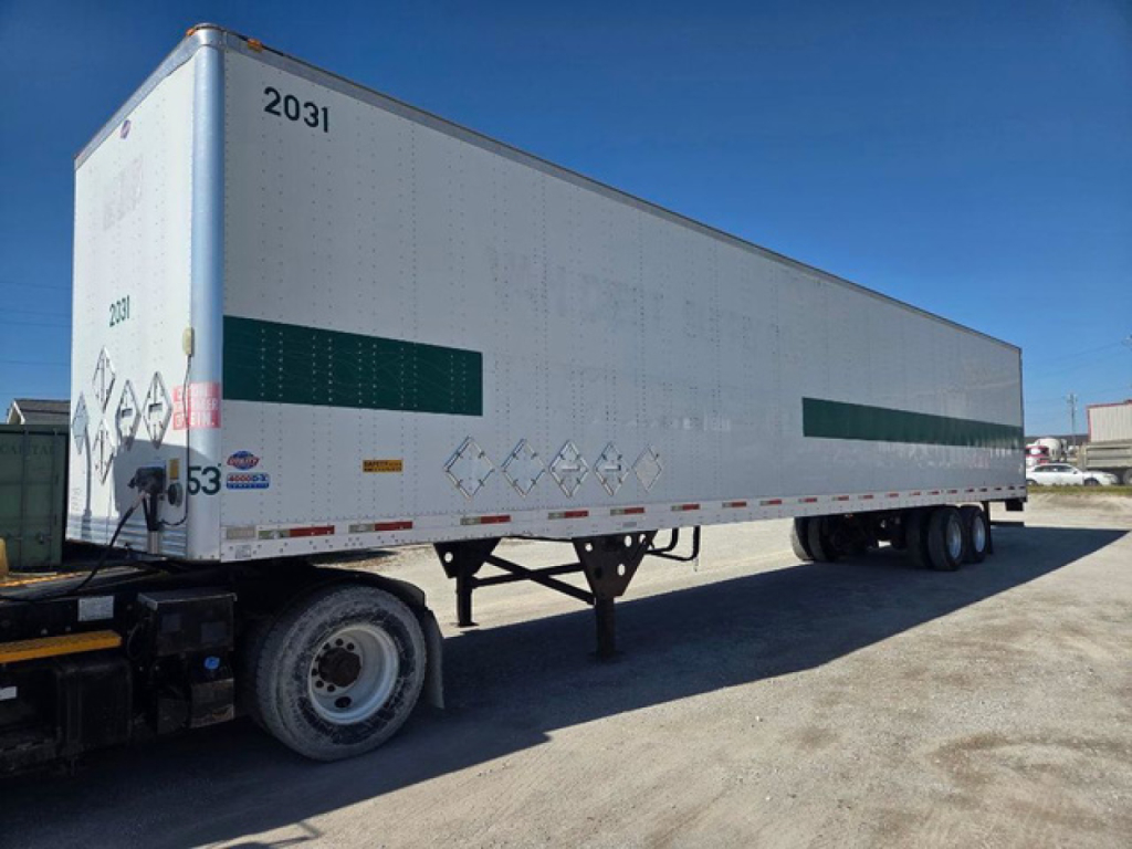 Trailer side view showing a white dry van trailer with green reflective panels and編 numbers, parked on a gravel lot.