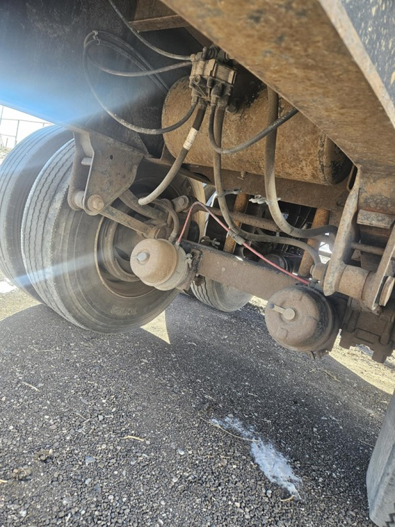 Rear underside of a Fruehauf flatbed trailer showing suspension components, air lines, and wheel hubs; rusted frame and hoses visible.