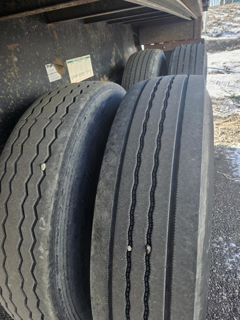 Flatbed trailer wheels and dual tires under the trailer with dirt and mud, tread patterns visible.
