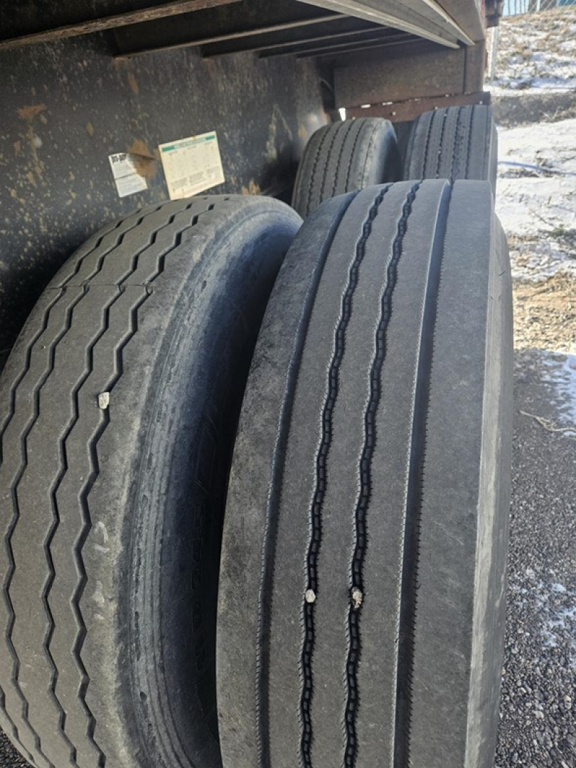 Flatbed trailer tires mounted under a Fruehauf steel flatbed, with multiple tires visible and some identification stickers on the frame.