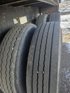 Flatbed trailer wheels and dual tires under the trailer with dirt and mud, tread patterns visible.
