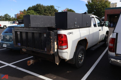 Truck bed of a white 2012 GMC Sierra 2500 4x4 with black steel toolbox and flatbed, rear view showing hitch, taillights, and service boxes.