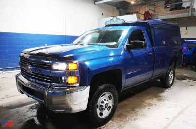 Chevrolet Silverado 2500HD pickup with ARE cap and slider in blue, front three-quarter view inside workshop.