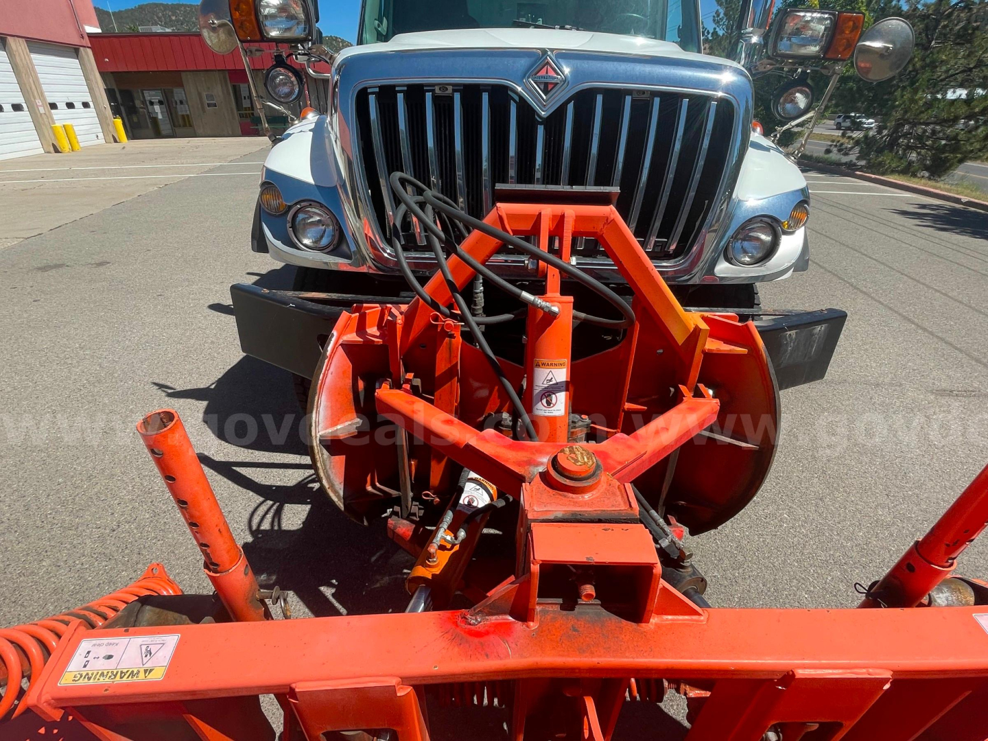 Front view of 2012 International 7400 dump truck with an orange snow plow/attachment in the foreground; grille and bumper visible.
