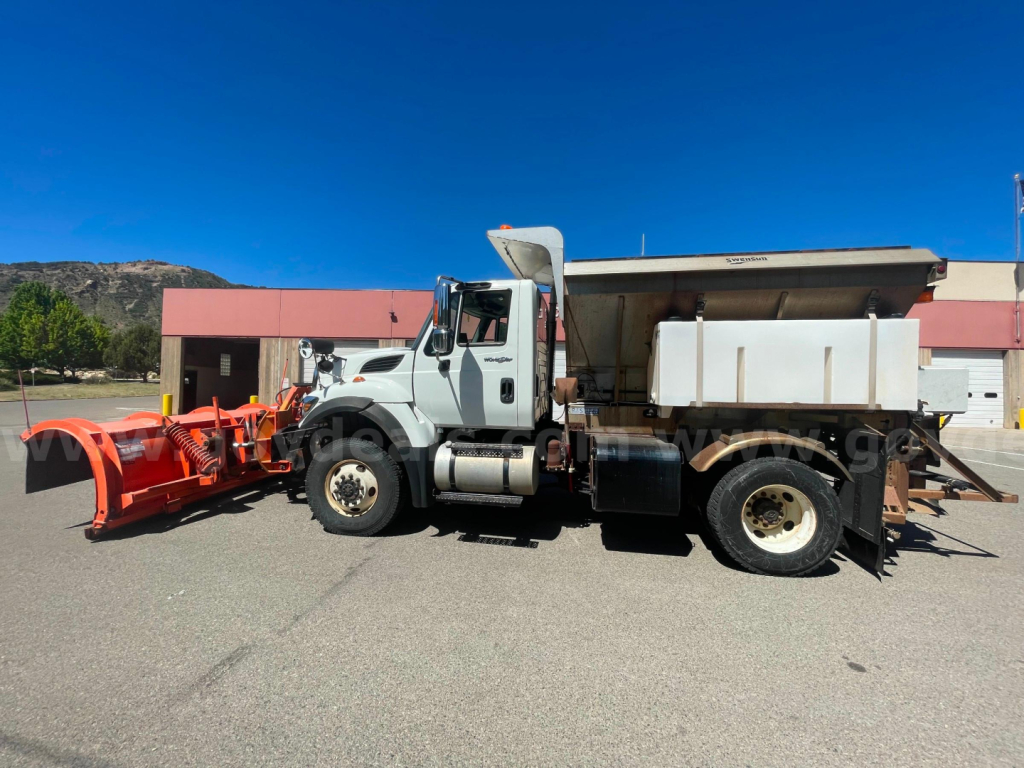 Dump truck with snowplow attachment in front, International 7400 cab, dump bed raised on a sunny day.