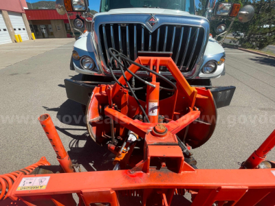 Front view of 2012 International 7400 dump truck with an orange snow plow/attachment in the foreground; grille and bumper visible.