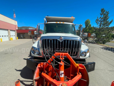 Dump truck front view of 2012 International 7400 with large grille, orange snowplow attachment and dual mirrors.