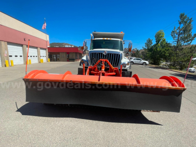 Front view of a 2012 International 7400 dump truck with a large red snow plow attachment in front, wheel arches, cab in background, dealership lot.