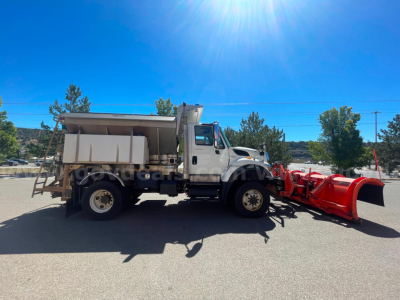 Truck in side view with a red snow plow attachment, dump bed, and International logo on cab. Clear blue sky, no visible text on equipment.