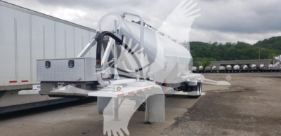 Pneumatic dry bulk trailer tank with front toolbox and circular piping showing on a gravel lot.