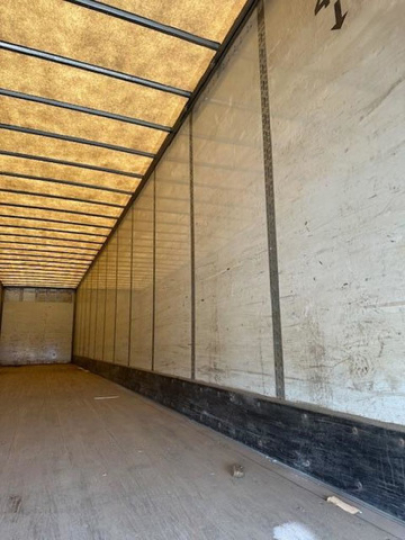 Van trailer interior showing long cargo area with wooden panel walls and metal rails along the ceiling.