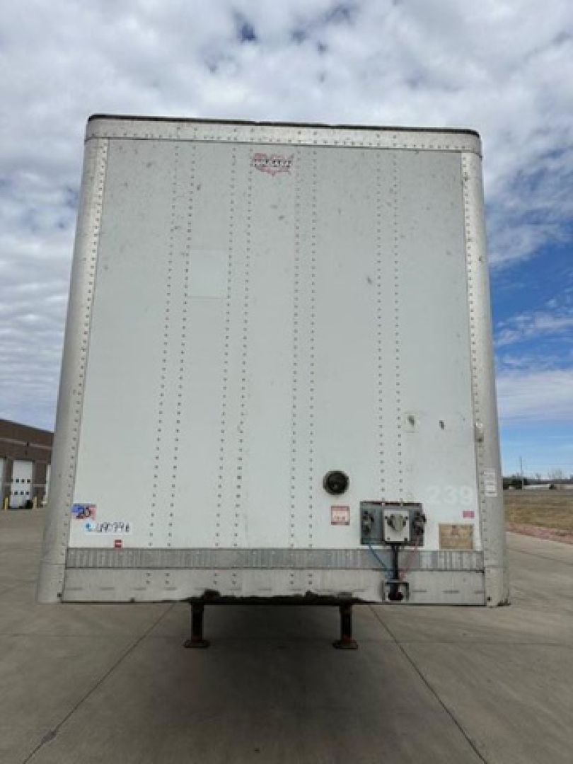 Trailer rear of a 2014 Wabash van trailer showing a blank white back door with a hitch and leveling legs in view.