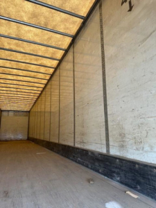 Van trailer interior showing long cargo area with wooden panel walls and metal rails along the ceiling.
