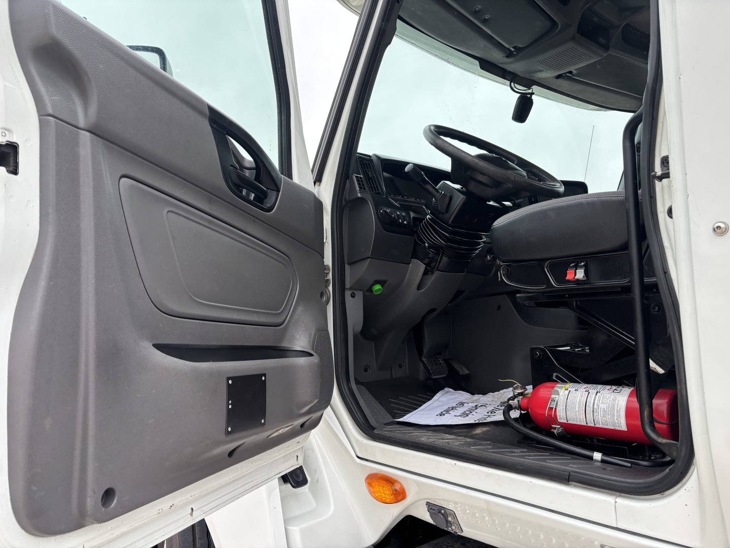 Cab interior of a 2019 International LT from the driver side, open door, steering wheel, dashboard, and a red fire extinguisher on the floor.