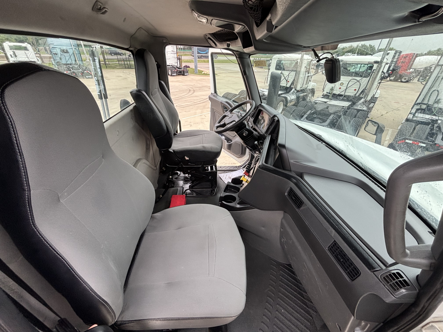 Interior view of a 2019 International LT cab from the passenger side, showing the driver seat, steering wheel, dashboard, and center console with gear selector and controls.