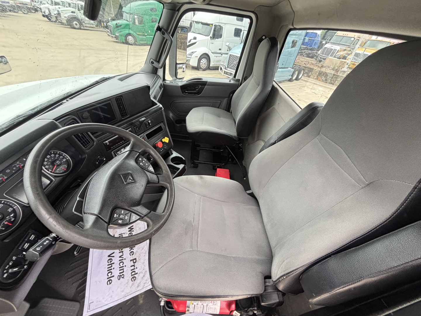 Truck cab interior of a 2019 International LT showing steering wheel, instrument cluster, driver's seat, and passenger seat with a view of the door and dashboard.