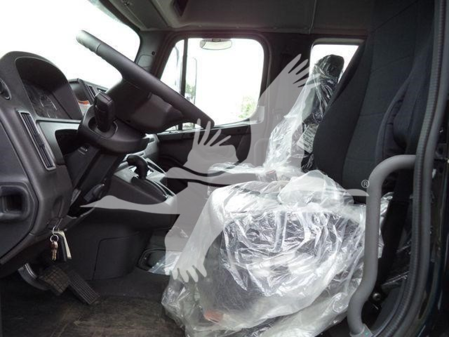 Freightliner M2 106 truck interior showing steering wheel, driver seat wrapped in plastic, and front cabin area.