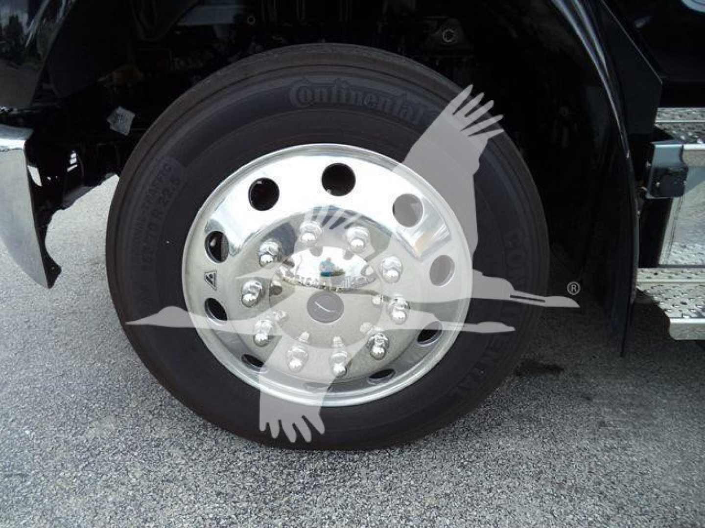 Wheel of a Freightliner truck showing a Continental tire and polished aluminum rim with lug nuts; part of the front wheel well and step visible.