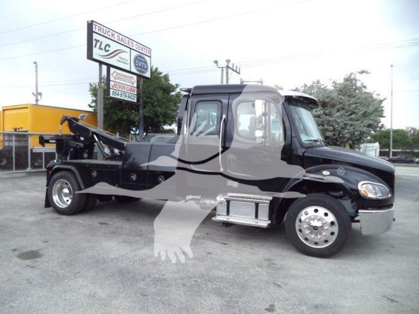 Freightliner M2 106 tow truck side view showing crane and winch in service bay with dealership sign in background.