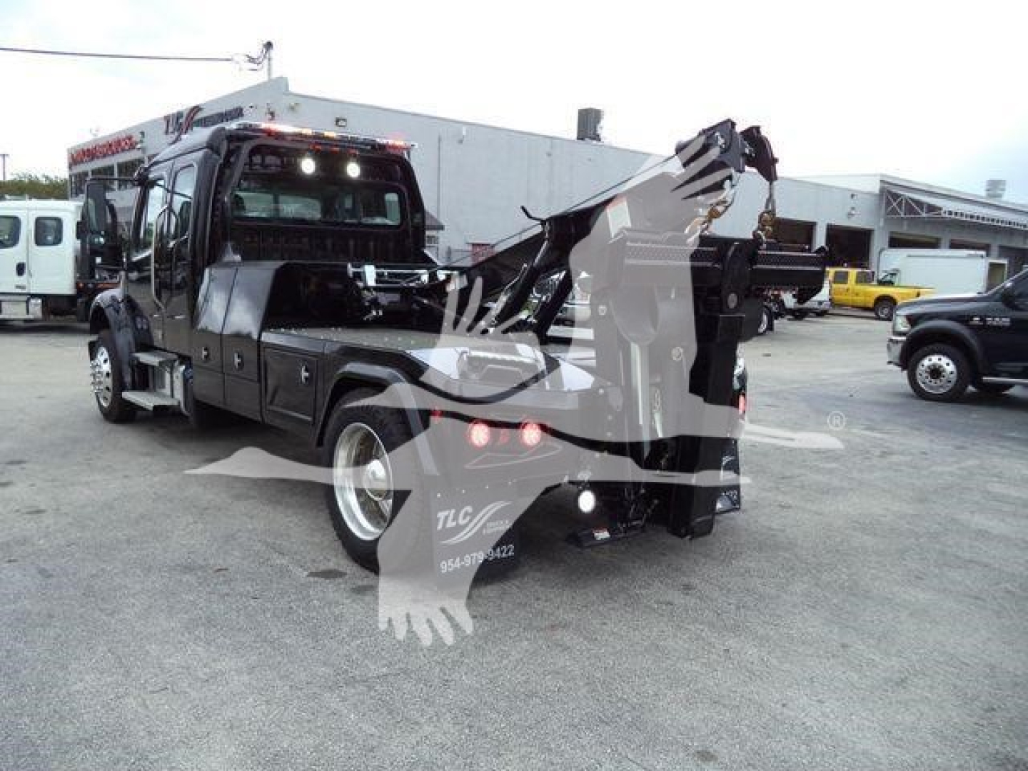 Truck rear view of a Freightliner M2 106 with a crane/winch setup, visible branding on side panels, and multiple warning decals.